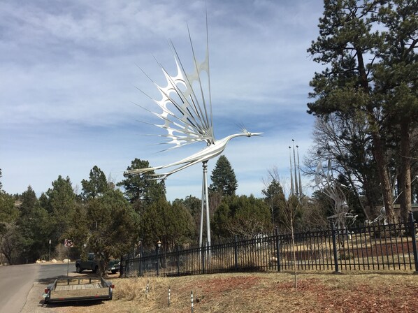 A metal sculpture resembling a bird in flight, surrounded by a fence and trees.