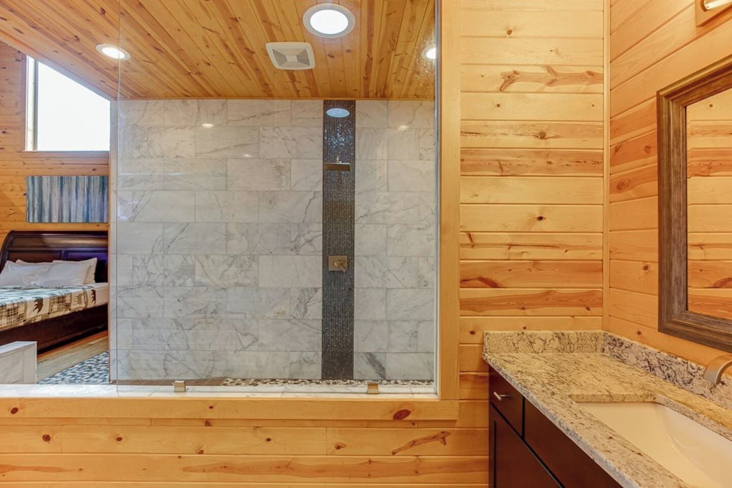 Interno di una baita in legno con bagno, dotato di doccia, letto e lavandino.