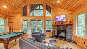 A wooden cabin with a pool table, leather sofa, and a fireplace.