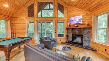 A wooden cabin with a pool table, leather sofa, and a fireplace.