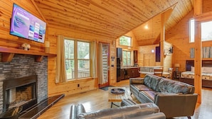 A cozy cabin interior with a fireplace, leather sofa, wooden floors, and a TV mounted on the wall.