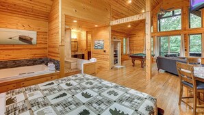 A log cabin with a large bed, a bathtub, a pool table, and a television.