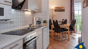 A modern kitchen with a built-in oven, a coffee maker, and a dining area with a table and chairs. - Villa Maria - Gabriele Whg, 02 - Maria 02 (Loddin)