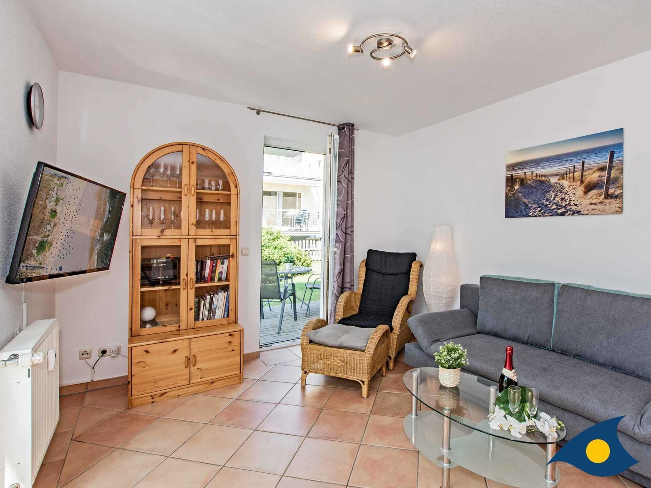 Een woonkamer met een bank, een glazen salontafel, een rieten fauteuil, een boekenkast en een televisie.