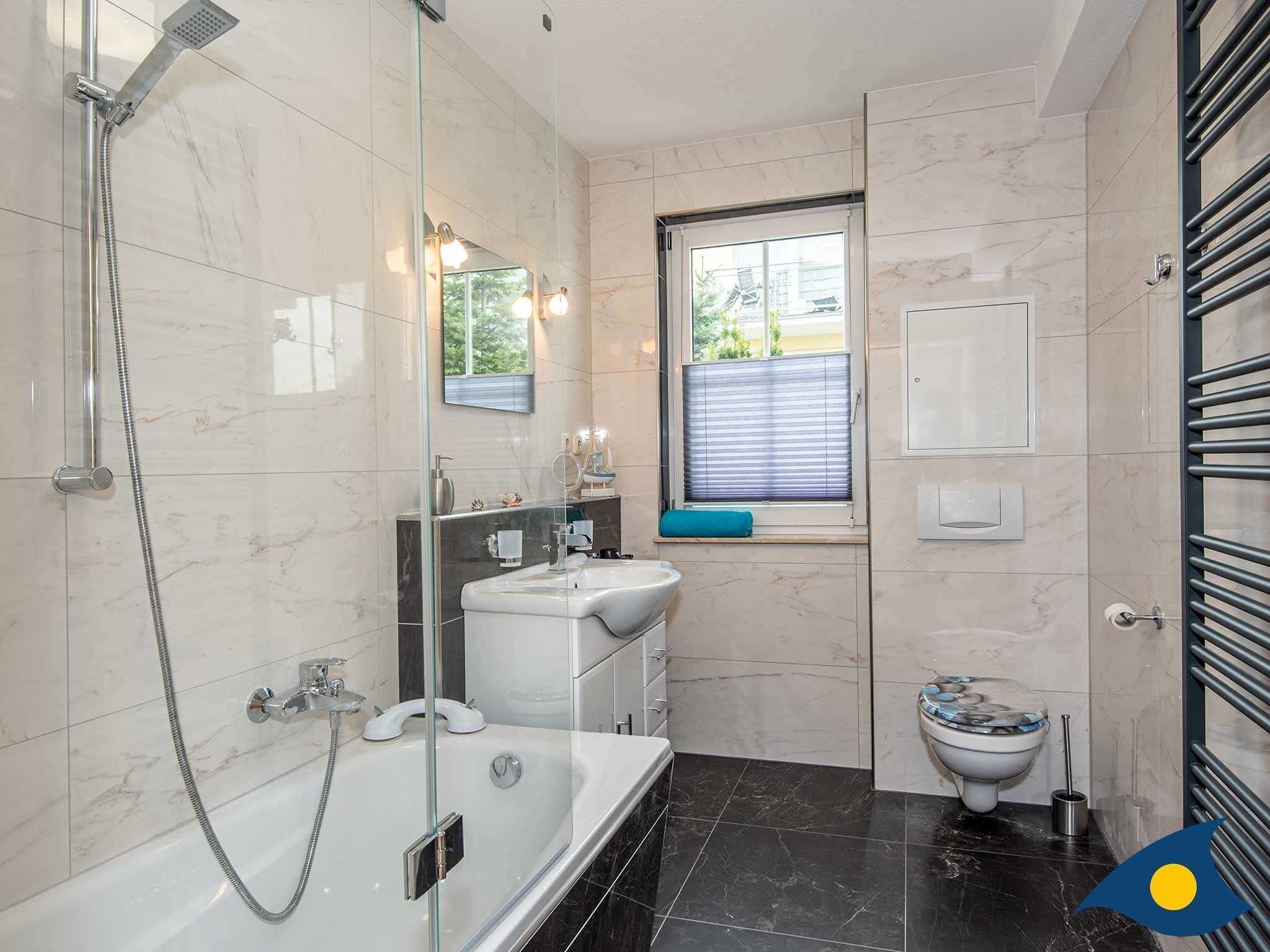 A modern bathroom with a glass-enclosed shower, a white sink, a toilet, and a window with blinds.