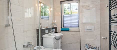 A modern bathroom with a glass-enclosed shower, a white sink, a toilet, and a window with blinds.