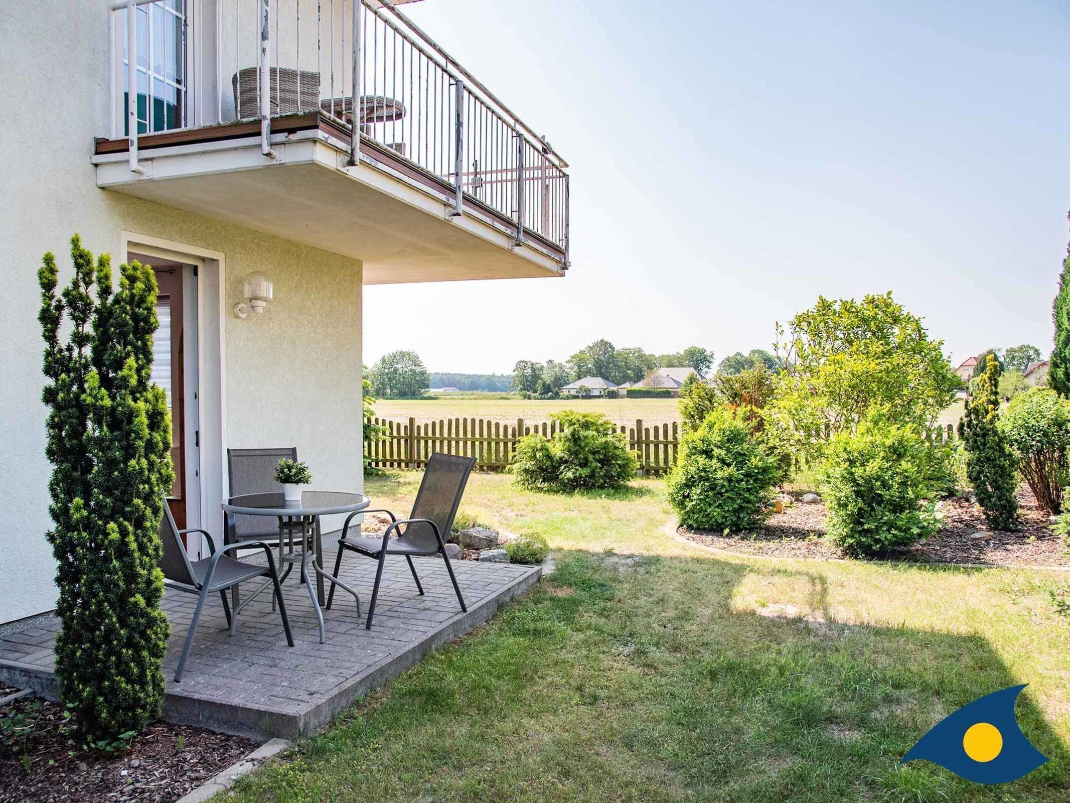 Una terrazza con tavolo e sedie, un piccolo giardino con diverse piante arbustive e vista su un paesaggio rurale.