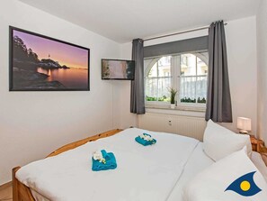A hotel room with a bed, a window with curtains, a wall-mounted TV, and a framed picture of a landscape.