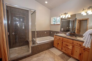 A modern bathroom with a glass-enclosed shower, a freestanding bathtub, wooden cabinetry, and a large mirror with lights.