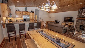 A spacious living area with a wooden dining table, bar stools, a sofa, and a television. - Sherman by Hauserman Rentals (Tahoma)