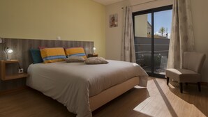 Un dormitorio con una cama grande, lámparas de noche, una silla y vistas a través de un ventanal corredero.