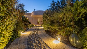 A pathway leading to a building with a circular structure, surrounded by dense greenery and illuminated by ground lights. - Villa Modigliani - Casarano (Casarano)