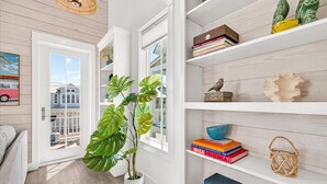 A hallway with a potted plant, a bookshelf with books and decorative items, and a door leading to a balcony. - Classic Home w/ Modern Flair near Beach Boardwalk, Pool & More Amenities! (Port Aransas)