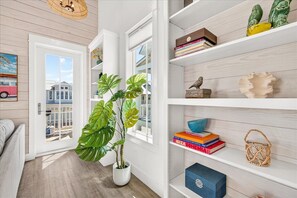 A hallway with a potted plant, a bookshelf with books and decorative items, and a door leading to a balcony. - Classic Home w/ Modern Flair near Beach Boardwalk, Pool & More Amenities! (Port Aransas)