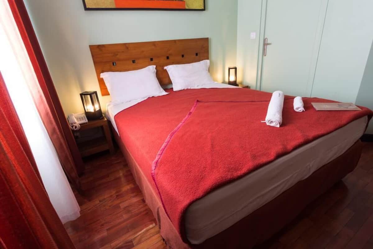 A neatly made bed with a red blanket, a wooden headboard, and a nightstand with a lamp and phone.