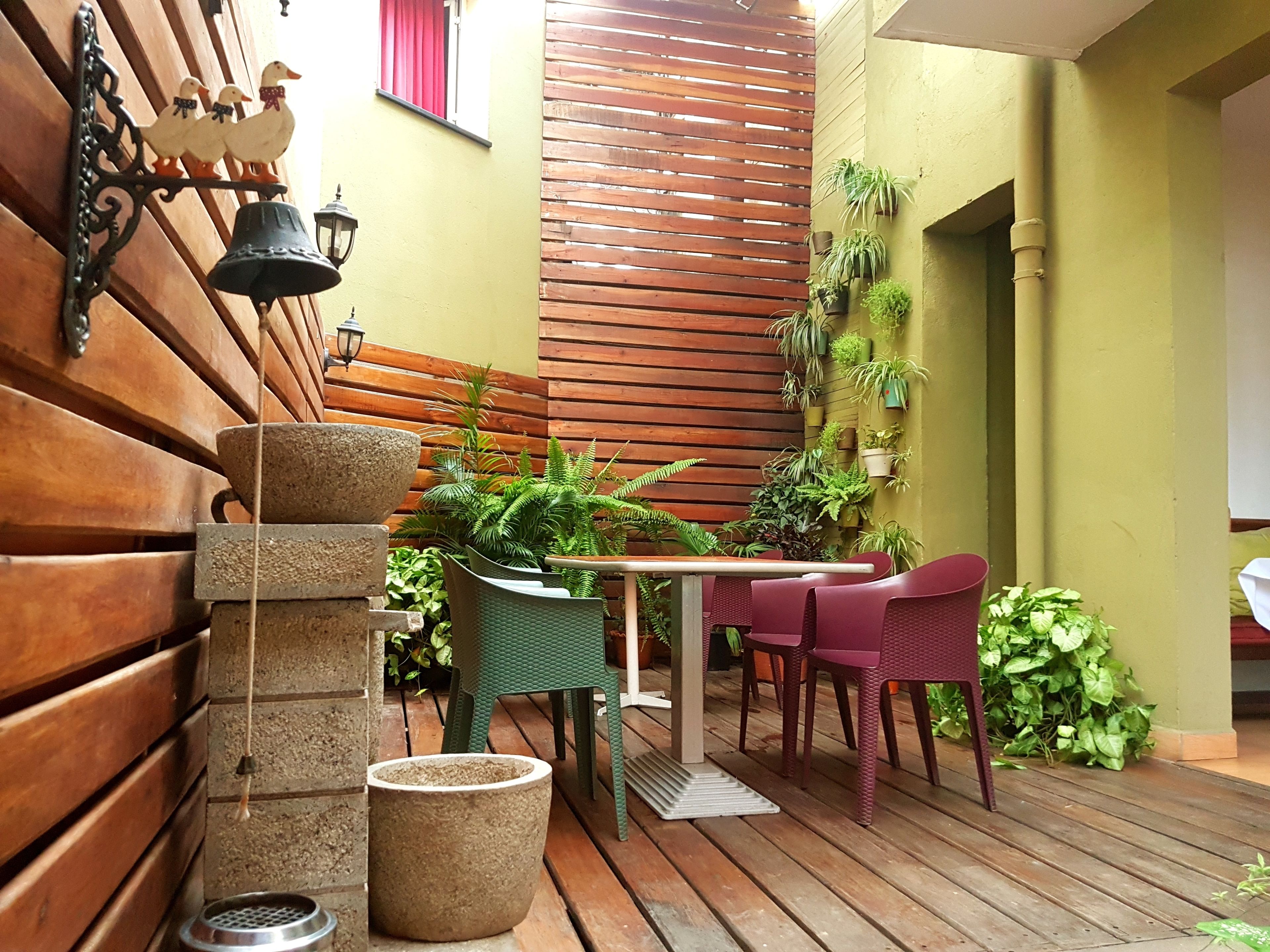 A wooden deck with a table and chairs, surrounded by potted plants and a wall-mounted bird decoration.