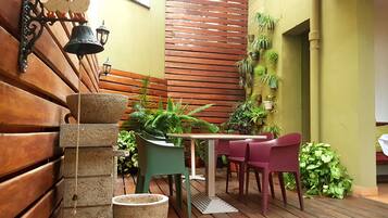 A wooden deck with a table and chairs, surrounded by potted plants and a wall-mounted bird decoration.
