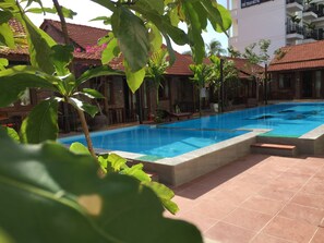 A swimming pool with a tiled deck, surrounded by buildings with red-tiled roofs and brick walls.