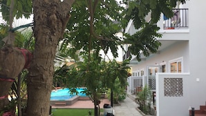 A courtyard with a swimming pool, a large planter with water lilies, and a tree with a rope tied around it. - May Bungalow (Mui Ne)