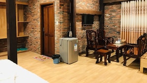 A room with a brick wall, wooden beams, a refrigerator, a wooden dining table with chairs, and a television mounted on the wall. - May Bungalow (Mui Ne)