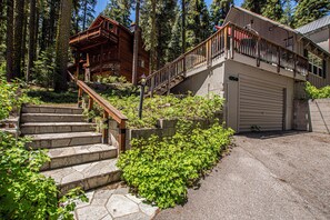 Een houten chalet met een stenen trap, een garage en een omliggend bos.