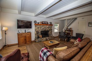 A living room with a stone fireplace, a television, a wooden cabinet, a sofa, and a staircase. - Hillhouse by Hauserman Rental Group (Homewood)