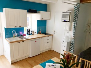 A compact kitchen with white cabinets, a wooden countertop, and a blue accent wall.