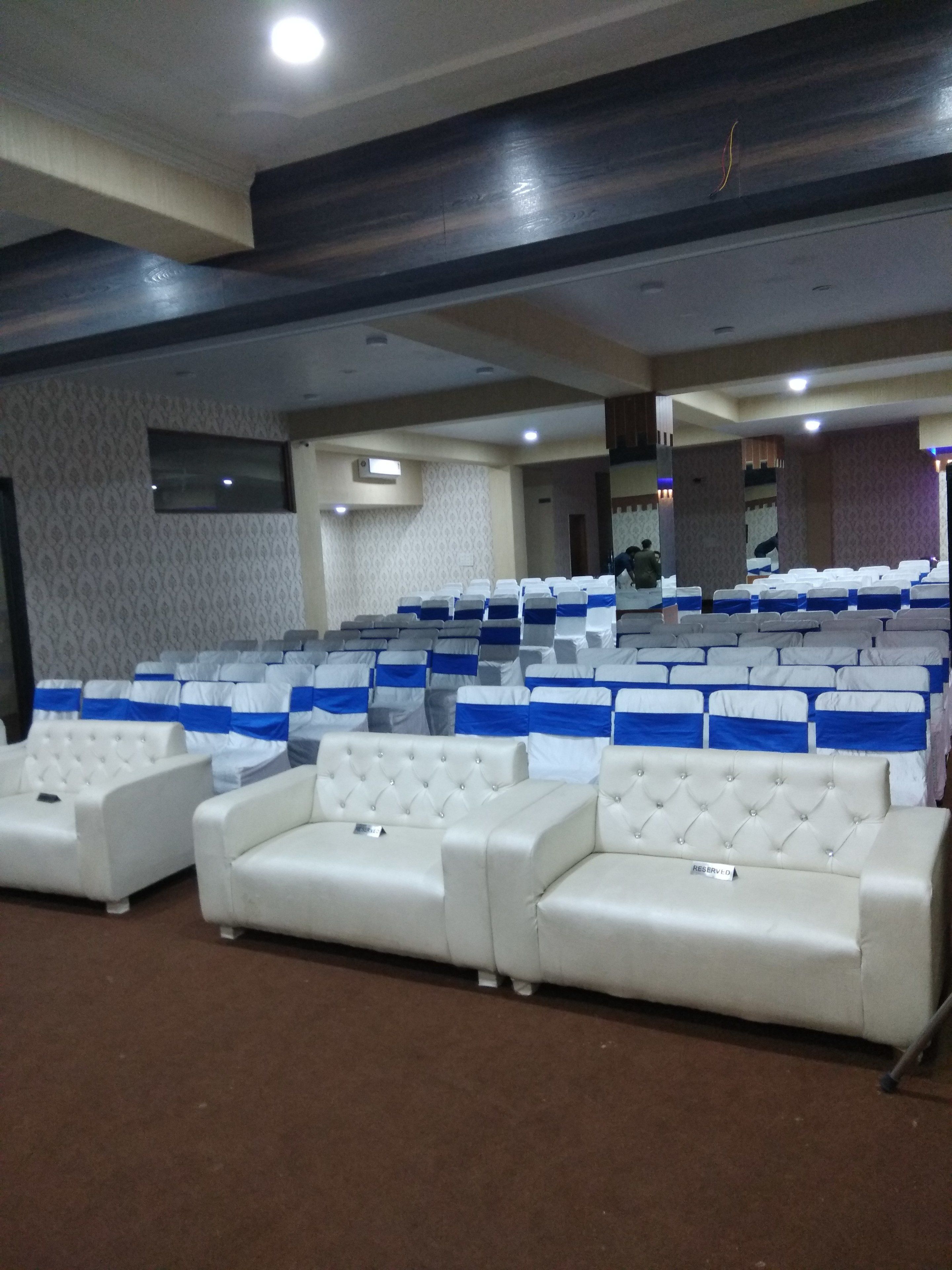 A conference room with rows of white chairs, some with blue sashes, and a few white cushioned seating areas.