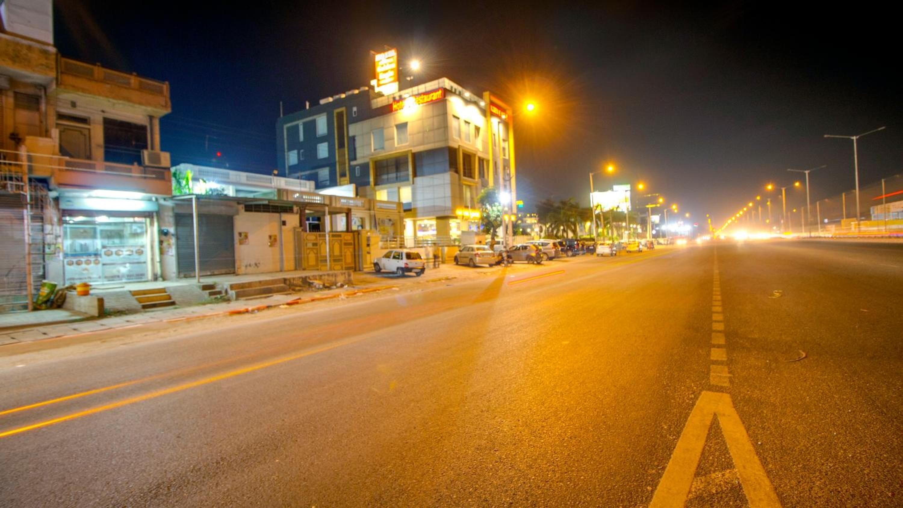 Nachtansicht einer Straße mit einem Hotel und Restaurant auf der linken Seite, einer gut ausgebauten Fahrbahn mit Fahrbahnmarkierungen und Straßenlaternen.