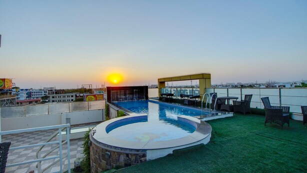 Una piscina en la azotea con vistas a la ciudad al atardecer, rodeada de mobiliario exterior y una zona cubierta.
