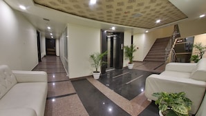 Un vestíbulo de hotel con un largo pasillo, dos sofás blancos, plantas en macetas y una escalera.