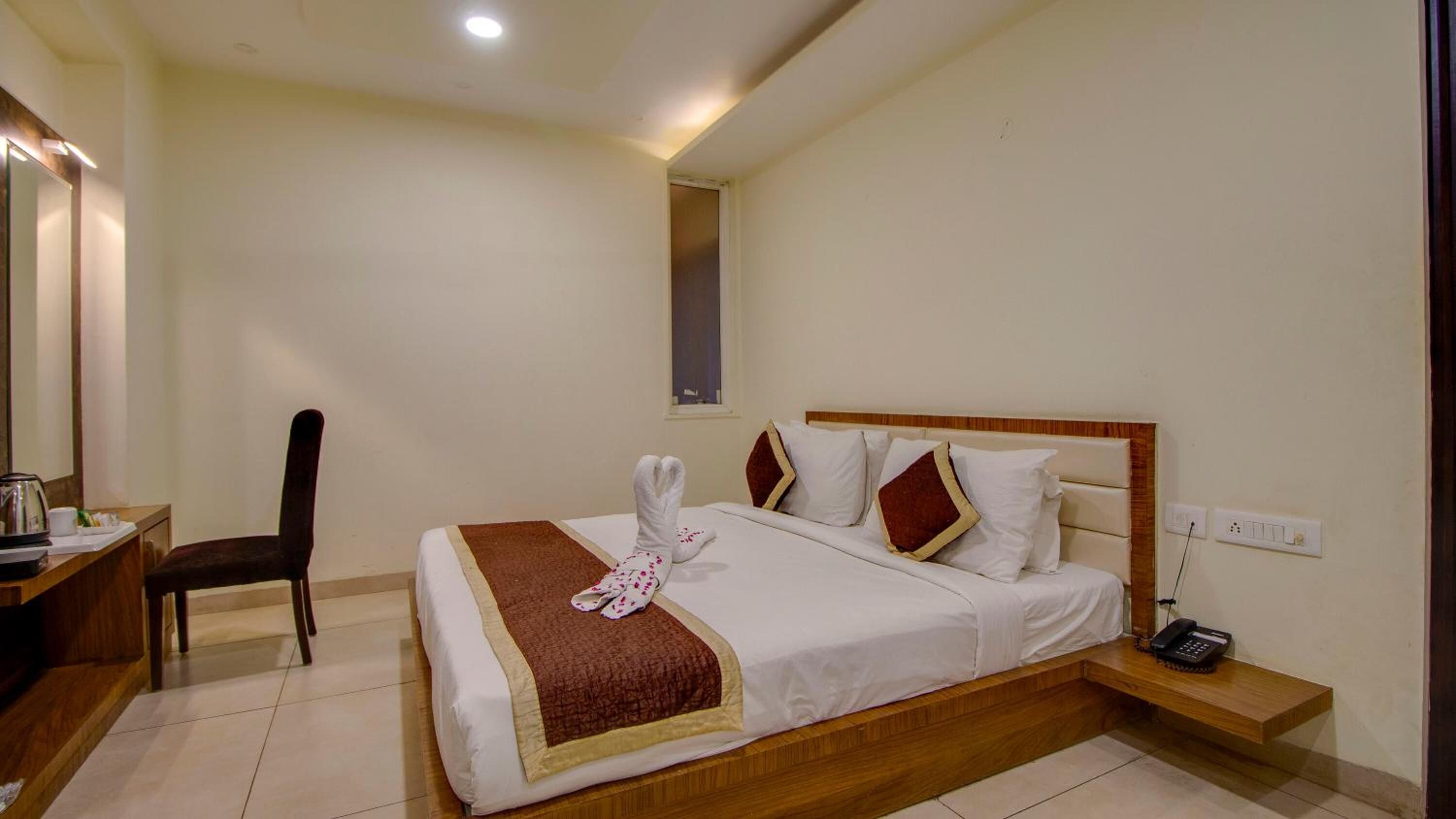 A hotel room with a bed, a desk, a chair, a bedside table, and a telephone.