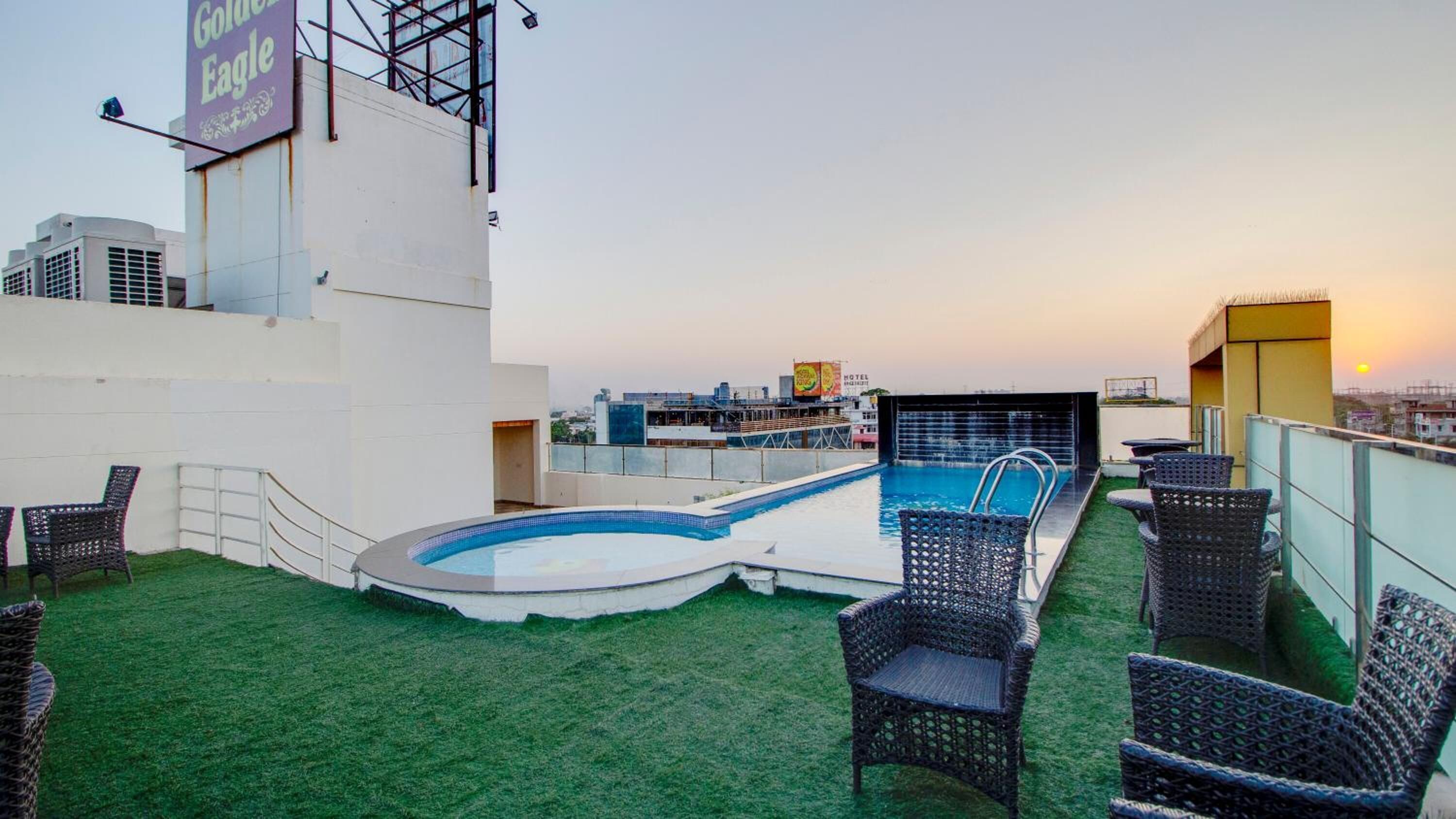 Zona de piscina en la azotea con vistas al horizonte urbano al atardecer, rodeada de sillas de mimbre y un cartel de 'Golden Eagle'.