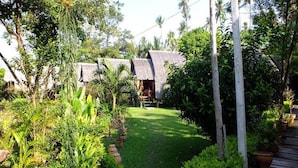 A garden with a pathway leading to thatched-roof huts, surrounded by lush greenery and potted plants. - Lanta Marina Resort (Ko Lanta)