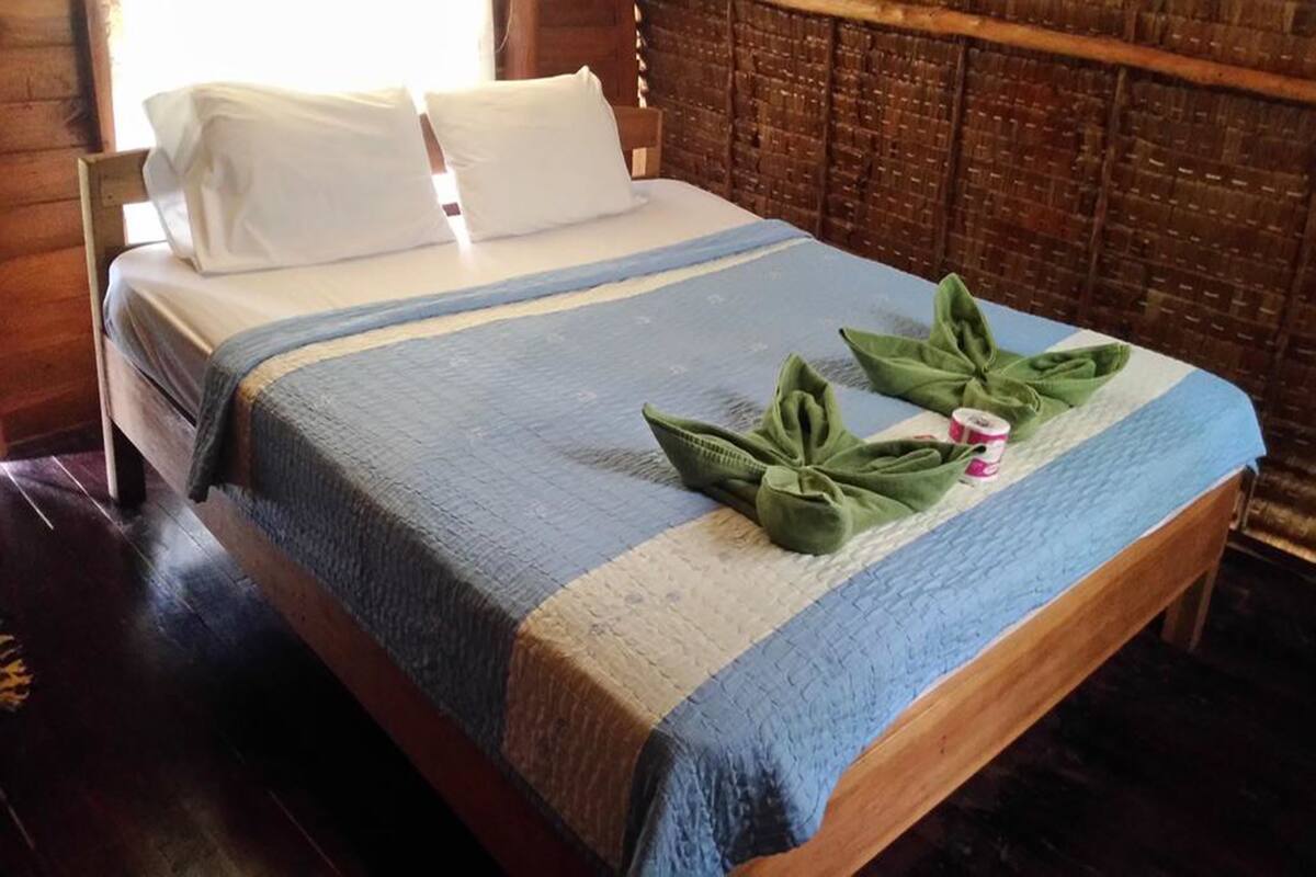 Ein Bett mit einer blau-weiß gestreiften Tagesdecke, zwei Kissen und einer Anordnung grüner Handtücher darauf.