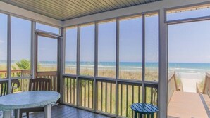 Un espace extérieur abrité, doté d’une table et de chaises, avec vue sur une plage.
