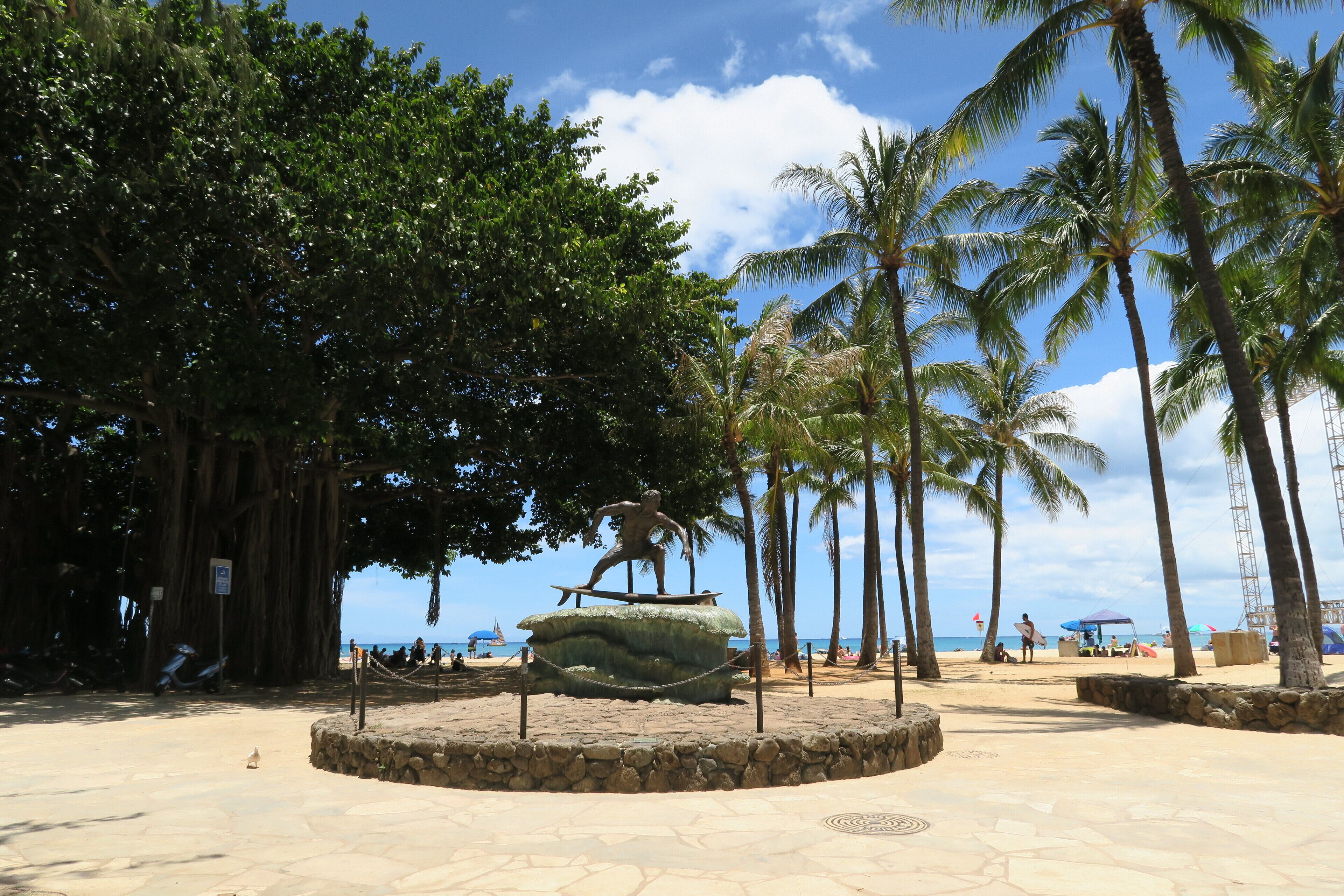 A beachside park with a statue, palm trees, and a stone pathway.