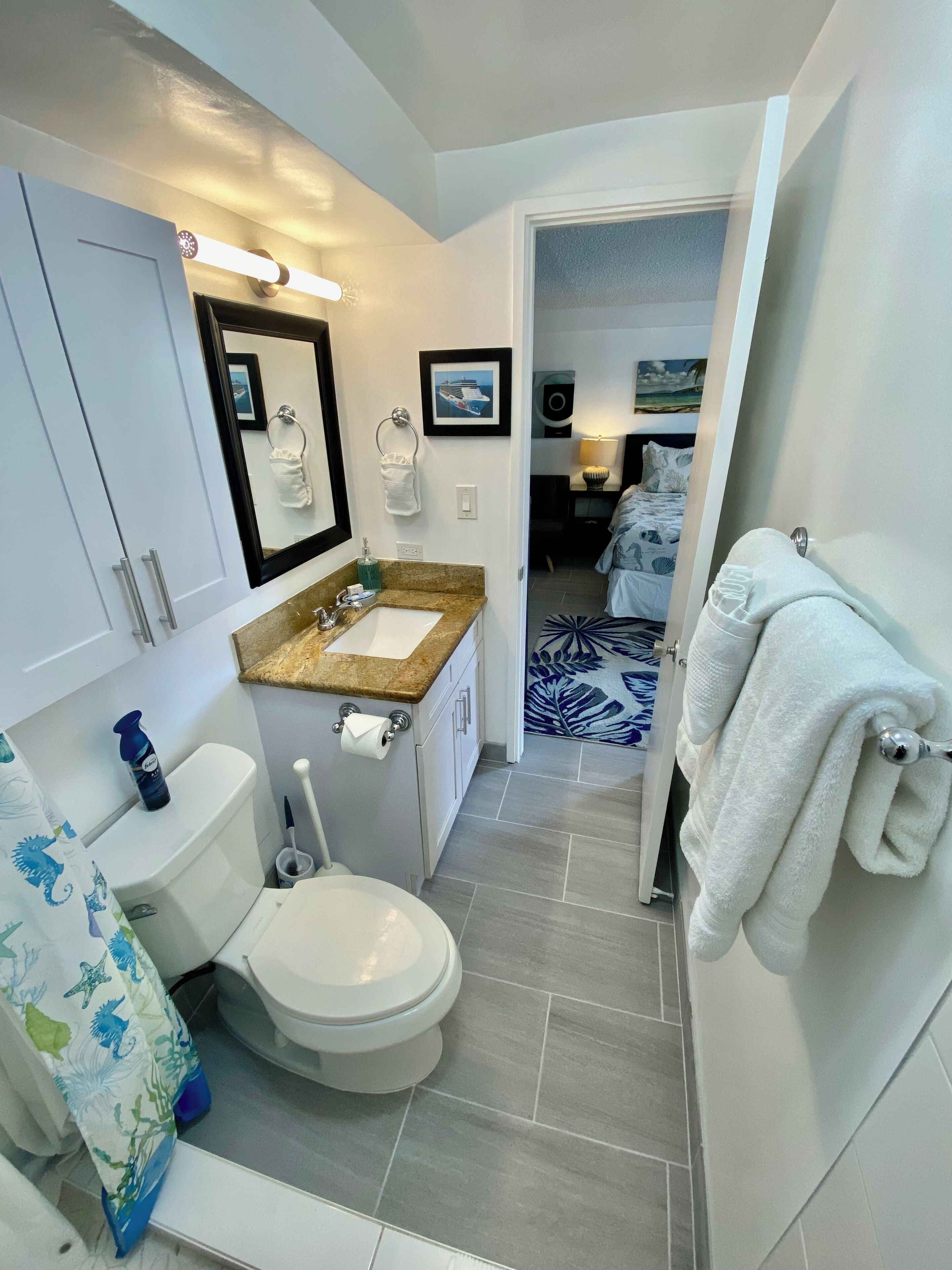 Une salle de bain moderne équipée de toilettes, d’un lavabo et d’une zone de douche. On y trouve un porte-serviettes avec une serviette suspendue, ainsi qu’un tableau encadré accroché au mur.