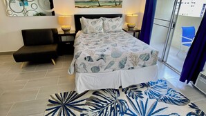 A bedroom with a bed, a nightstand, a chair, a large window, and a view of the outside. - Aloha Suite Near the Sea II, 3 Block Walk to Beach (Honolulu)