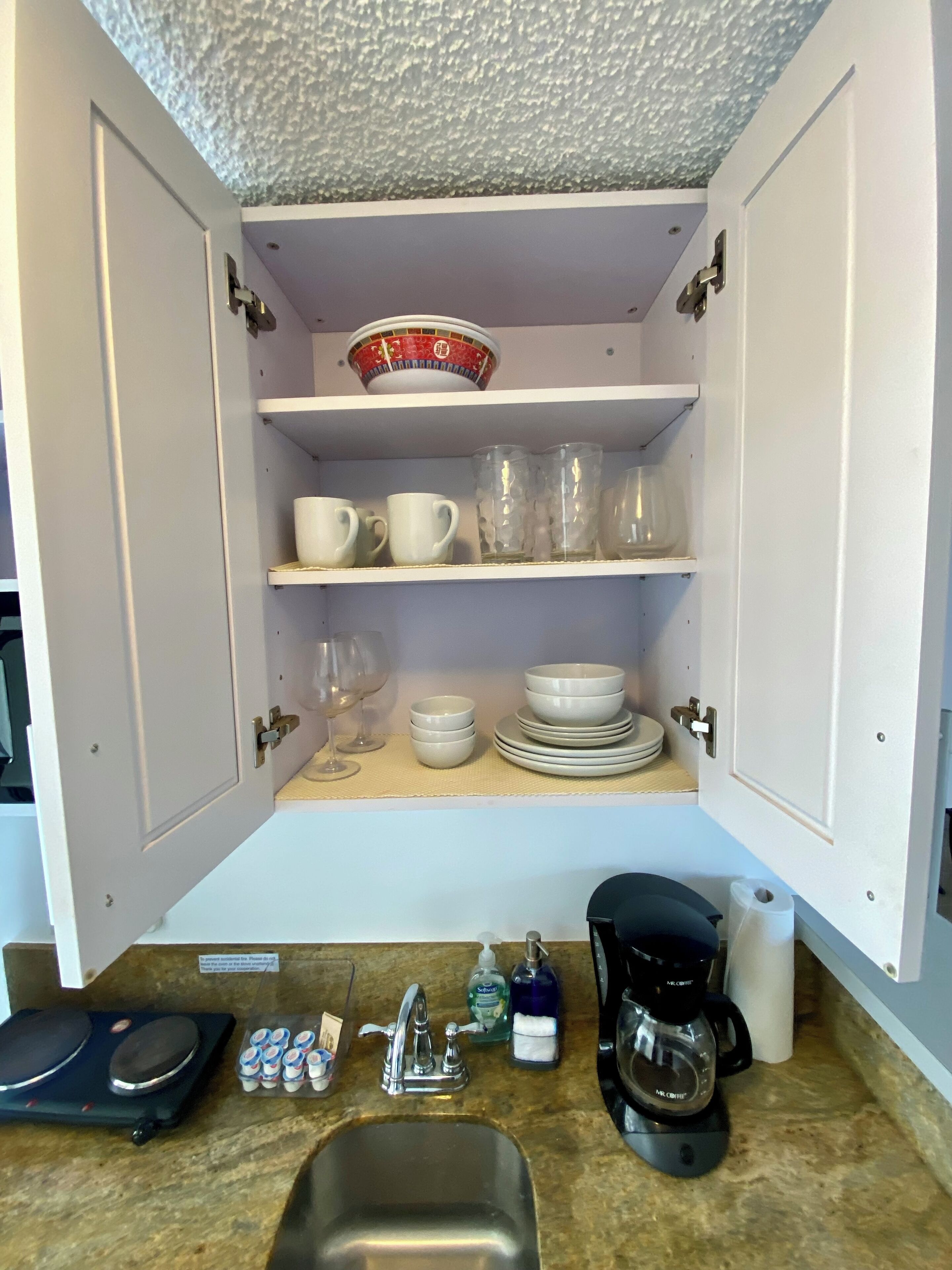Una cocina con mostrador, lavamanos y un mueble con vajilla y vasos.