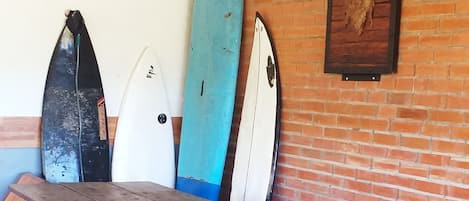 Una mesa de madera rústica con bancos, rodeada de tablas de surf sobre un muro de ladrillo.
