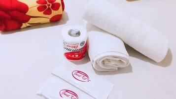 En snyggt bäddad säng med blommiga kuddar, en hoprullad handduk, en flaska lotion och en väska med gästprodukter.