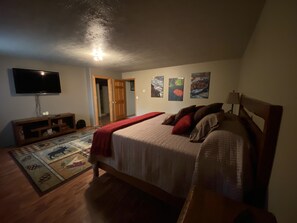 A bedroom with a bed, a TV, a wooden dresser, and a door leading to another room.