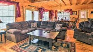 A cozy log cabin interior with a large sectional sofa, a coffee table, and a dining area with a chandelier. - Lazy Bear Lodge: 6BR, Theater,Spa,Pool,Game room! (Pigeon Forge)