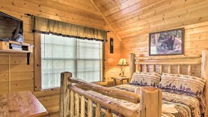 A log cabin room with a wooden bed, a small table, and a window with blinds. - Lazy Bear Lodge: 6BR, Theater,Spa,Pool,Game room! (Pigeon Forge)
