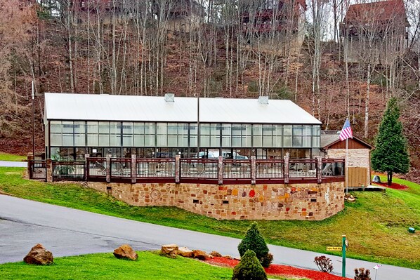 Un chalet doté de fondations en pierre et d’une façade en verre, entouré d’une terrasse en bois et d’un mât portant un drapeau.
