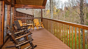 Eine Holzdielen-Terrasse mit Schaukelstühlen und einem Tisch, mit Blick auf ein bewaldetes Gebiet.