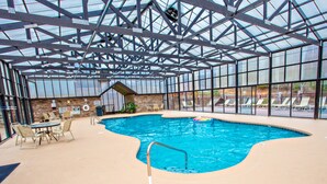 Ein Hallenbad mit Glasdecke, Liegestühlen und einer Steinwand.