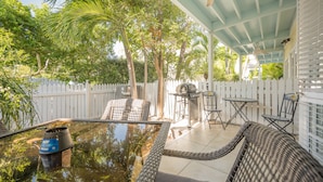 A covered patio with a pool table, outdoor furniture, and a white picket fence.