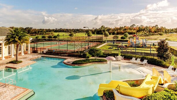 Ein Schwimmbecken mit Rutsche, umzäunt, und ein Tennisplatz im Hintergrund.